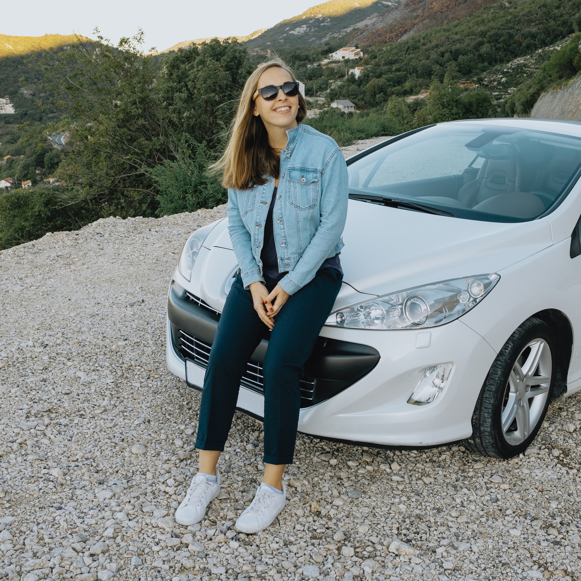 Smiling woman in sunglasses sitting near a car