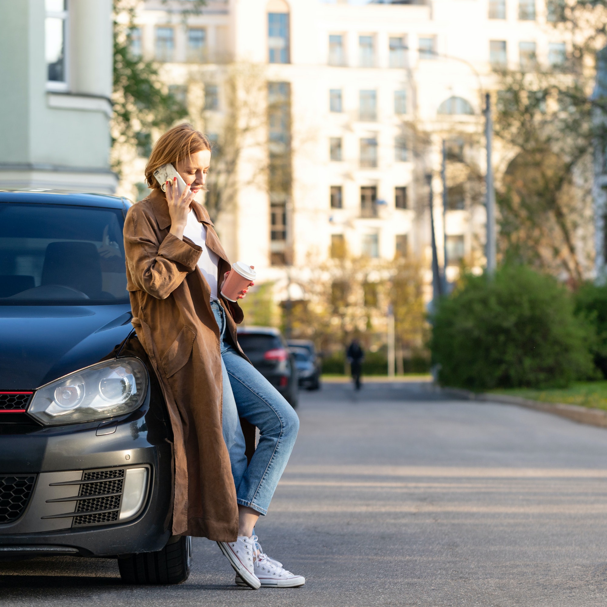 woman standing near her car and talking on the phone, holding a coffee cup